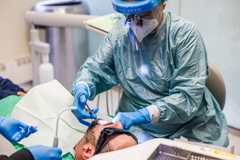 a man in a hospital mask is on a computer  at RTC Dental in Ashburn for RTC Dental Reston services.