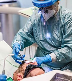 a man in a hospital mask is on a computer  at RTC Dental in Ashburn for RTC Dental Reston services.